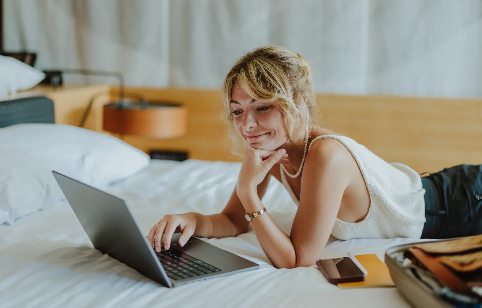 junge Frau auf dem Hotelbett mit Laptop nutzt die Partnerschaft zwischen Marriott Bonvoy und Emirtaes Skywards
