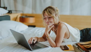 junge Frau auf dem Hotelbett mit Laptop nutzt die Partnerschaft zwischen Marriott Bonvoy und Emirtaes Skywards