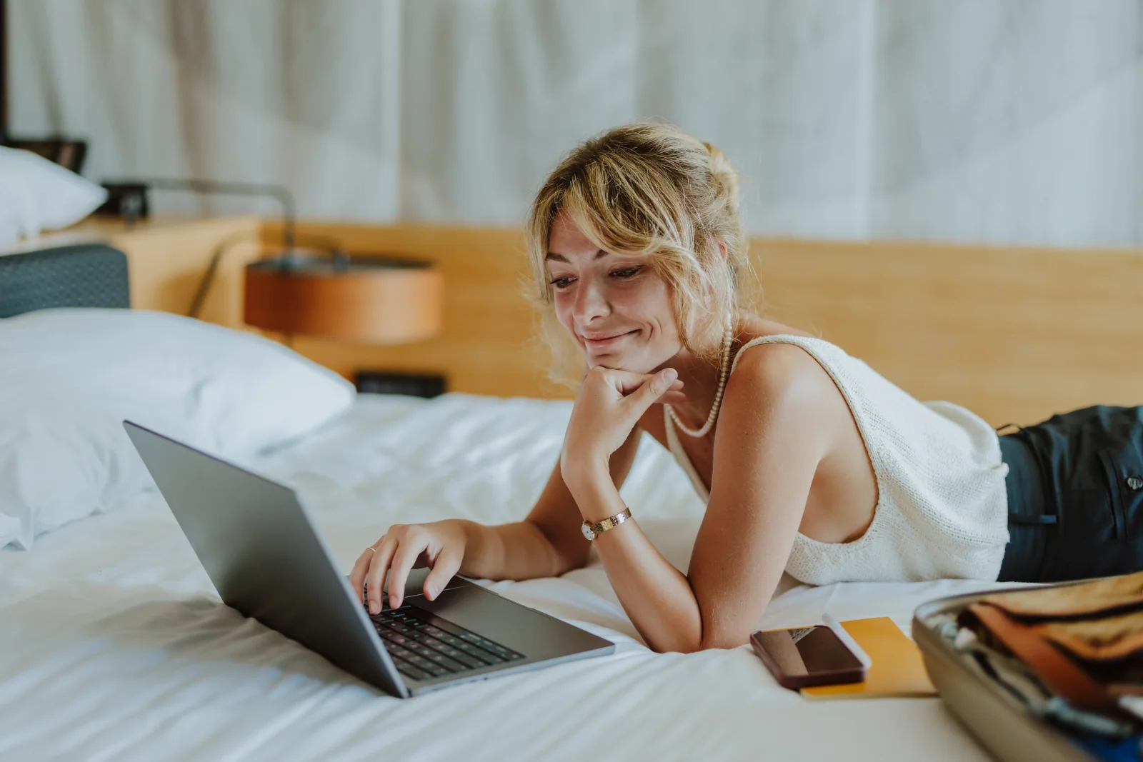 junge Frau auf dem Hotelbett mit Laptop nutzt die Partnerschaft zwischen Marriott Bonvoy und Emirtaes Skywards