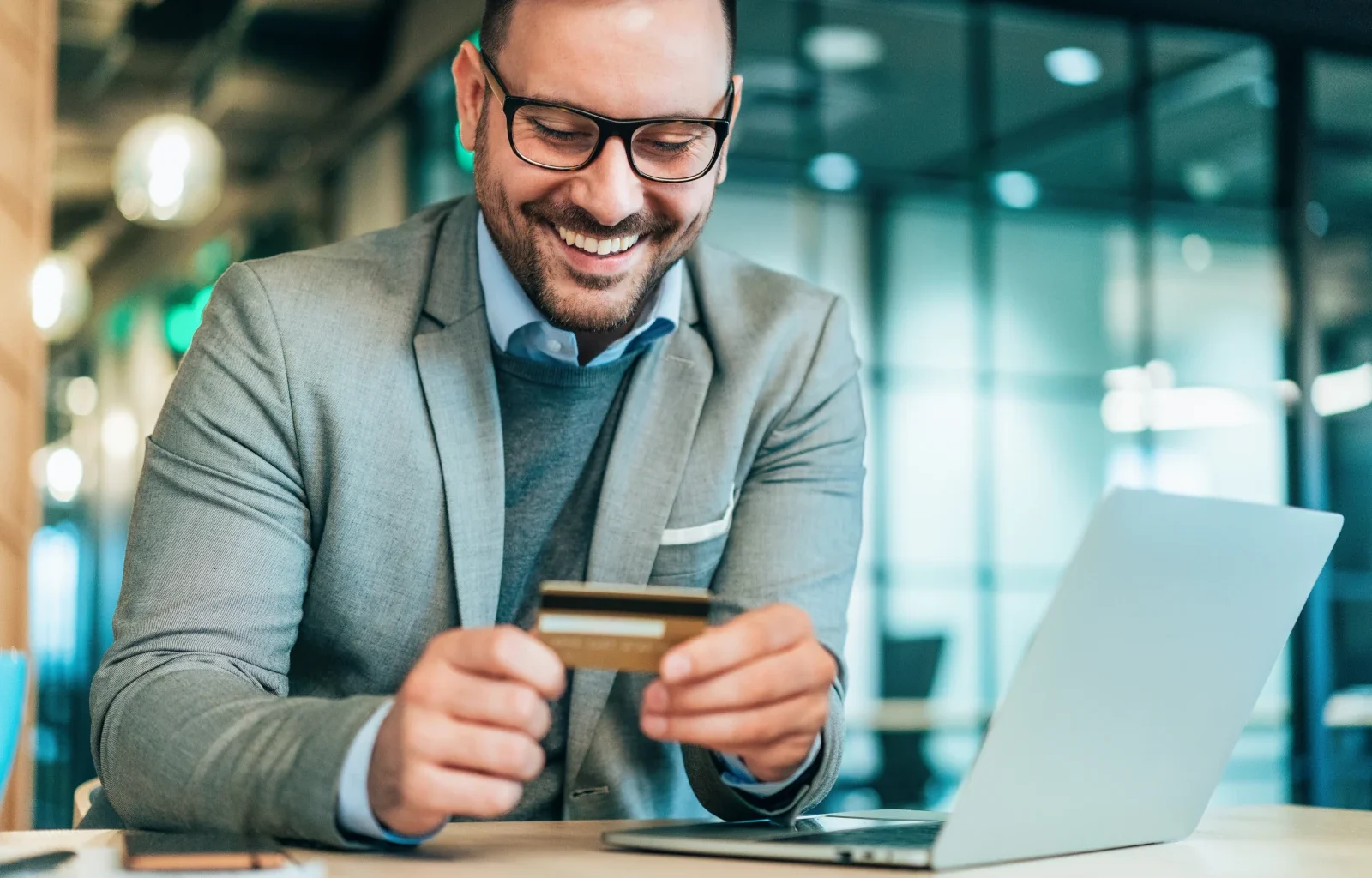 junger Geschäftsmann mit einer American Express Business Gold Card am Laptop