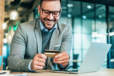 junger Geschäftsmann mit einer American Express Business Gold Card am Laptop