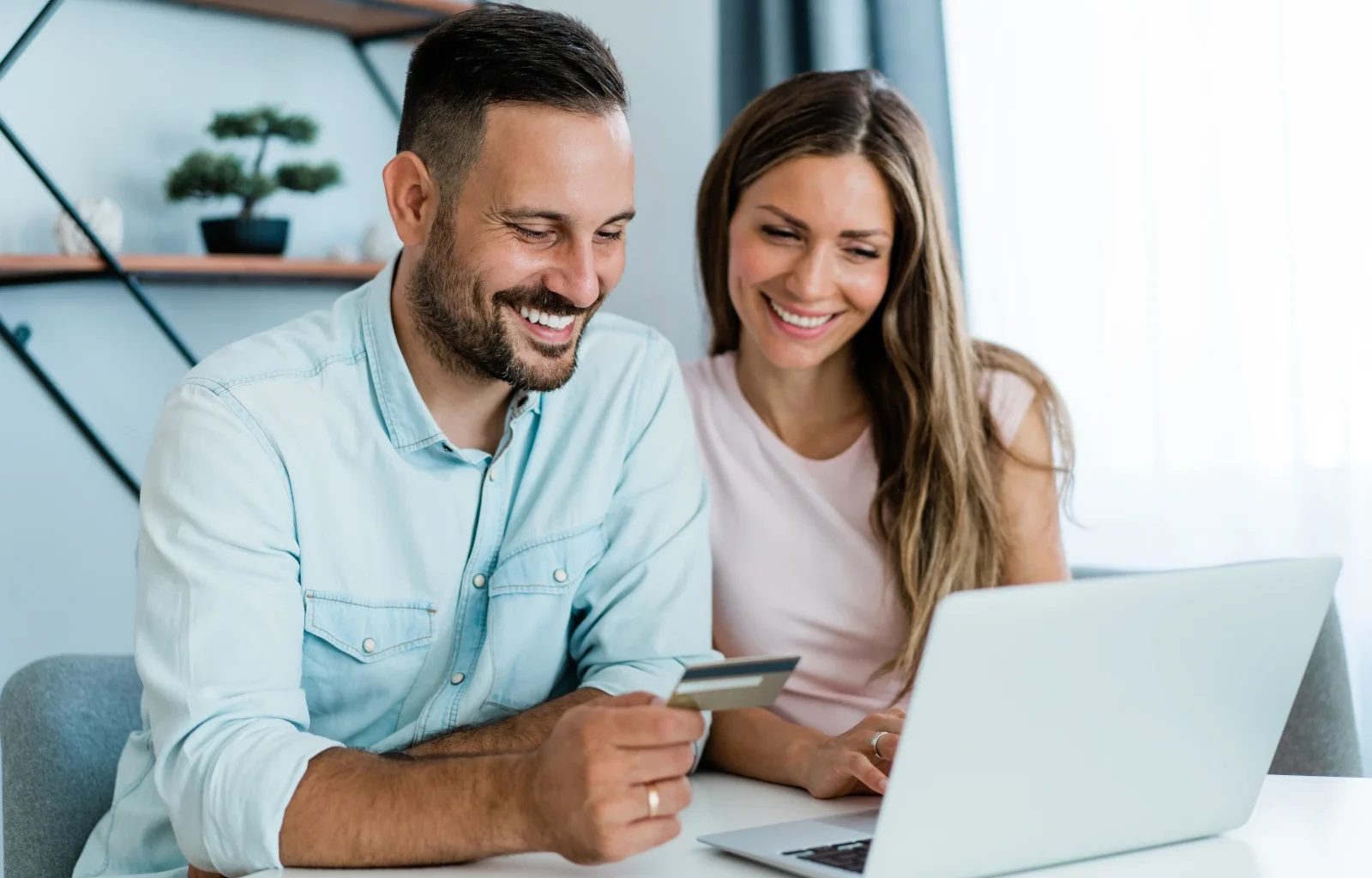 Junges, fröhliches Paar, das zu Hause online einkauft. Kombinieren Sie Online-Shopping mit Kreditkarte und Laptop.