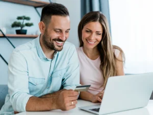 Junges, fröhliches Paar, das zu Hause online einkauft. Kombinieren Sie Online-Shopping mit Kreditkarte und Laptop.