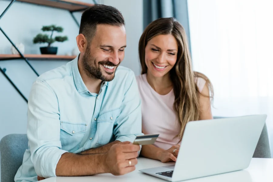 Junges, fröhliches Paar, das zu Hause online einkauft. Kombinieren Sie Online-Shopping mit Kreditkarte und Laptop.