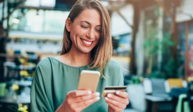 lächelnde Frau hält eine Kreditkarte in der einen und ihr iPhone in der anderen Hand