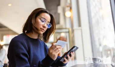 Frau mit Brille hält eine Kreditkarte und ein Smartphone in den Händen