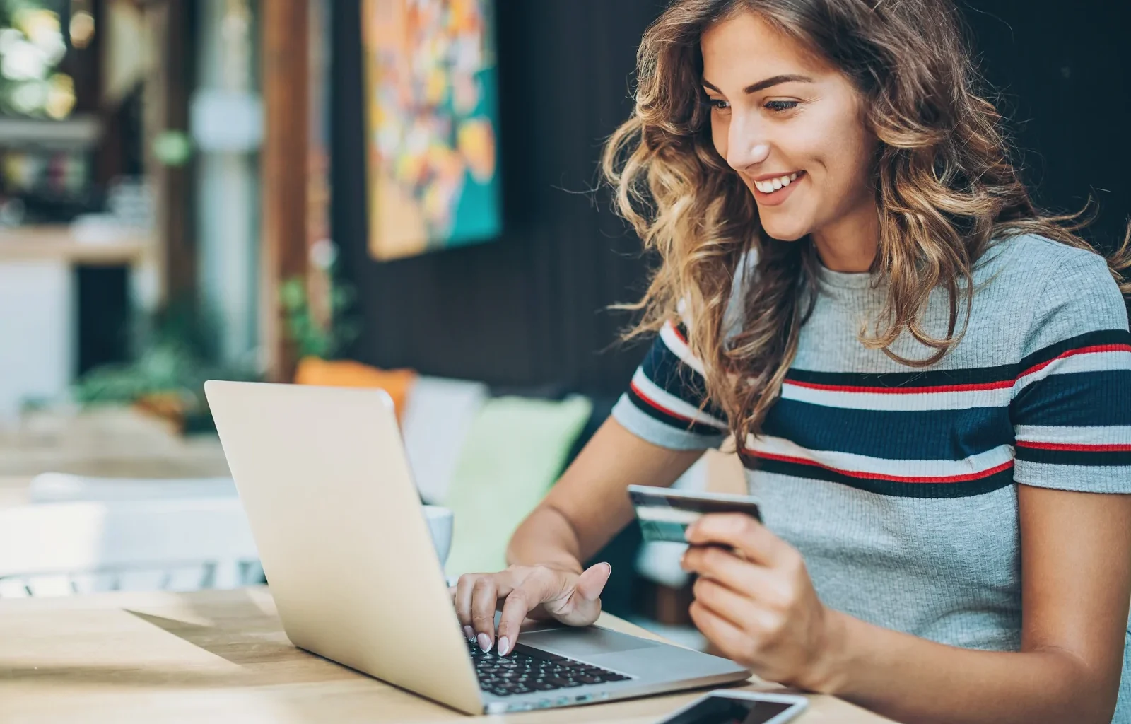 lächelnde Frau hält eine Kreditkarte in der Hand vor ihrem Laptop