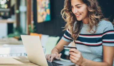 lächelnde Frau hält eine Kreditkarte in der Hand vor ihrem Laptop