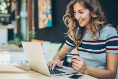 lächelnde Frau hält eine Kreditkarte in der Hand vor ihrem Laptop