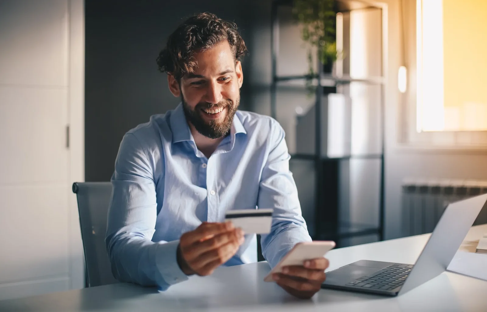 attraktiver Geschäftsmann mit Kreditkarte in der Hand kauft online etwas auf seinem Smartphone