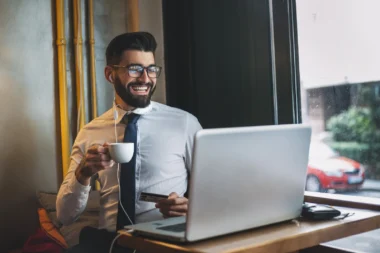 junger Geschäftsmann mit Kaffee und Kreditkarte vor seinem Laptop