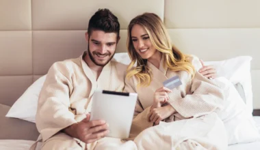 Junges Paar in einem Bett eines Luxushotels beim Online-Shopping mit Kreditkarte