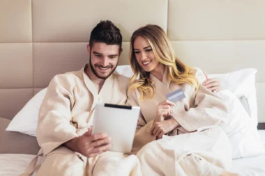 Junges Paar in einem Bett eines Luxushotels beim Online-Shopping mit Kreditkarte