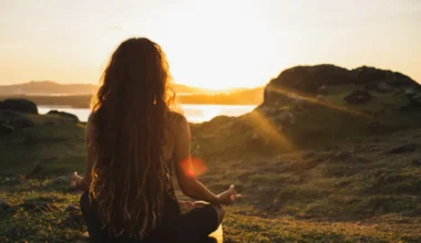 junge Frau meditiert auf einem Berg beim Sonnenaufgang