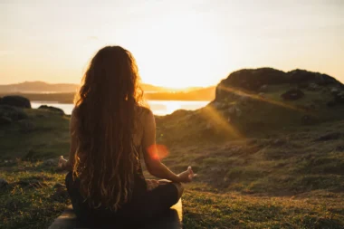 junge Frau meditiert auf einem Berg beim Sonnenaufgang