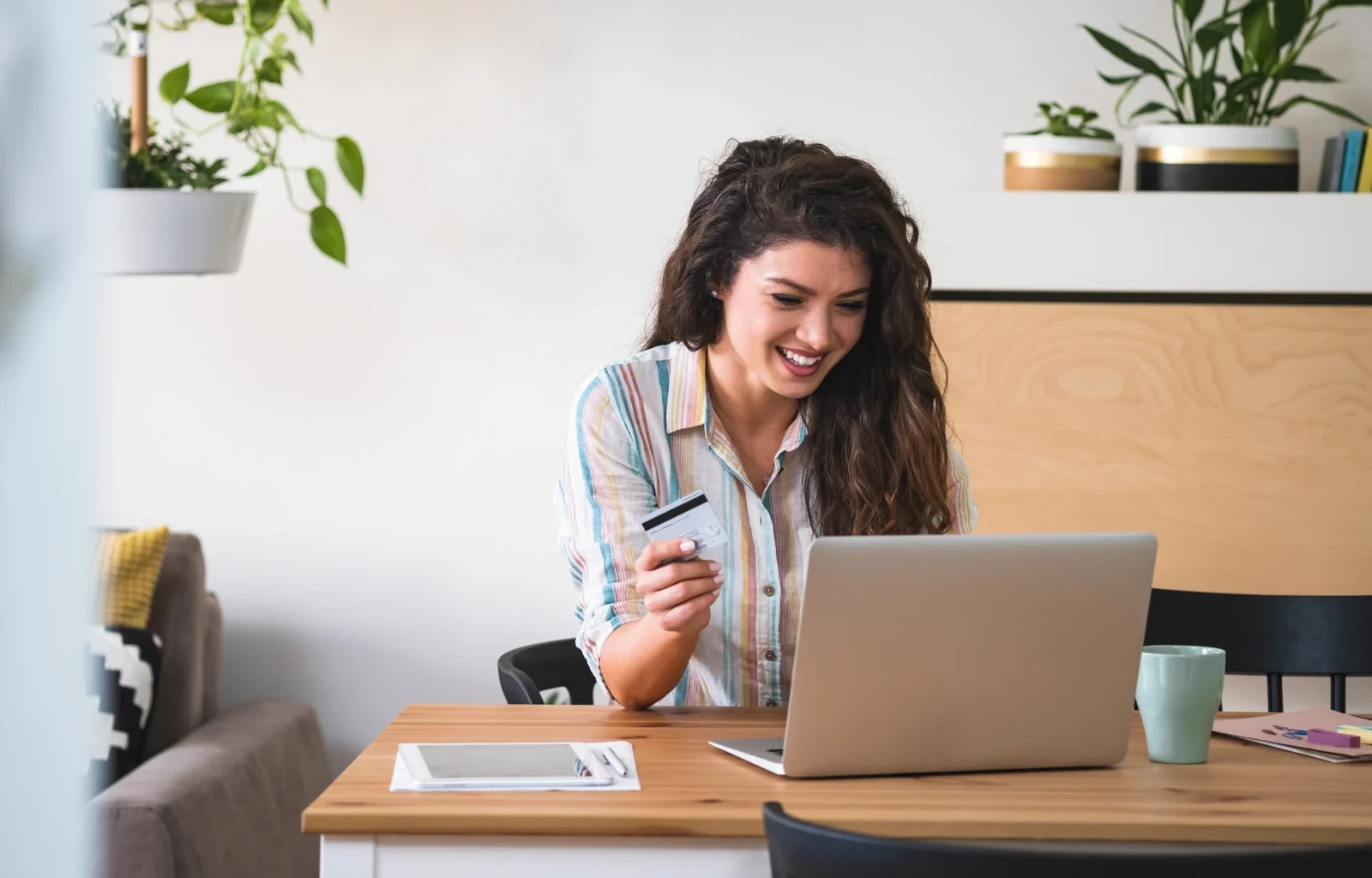 Junge Frau, die mit Kreditkarte am Schreibtisch sitzt und Geld beim Online-Shopping ausgibt