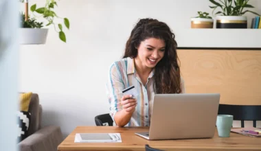 Junge Frau, die mit Kreditkarte am Schreibtisch sitzt und Geld beim Online-Shopping ausgibt