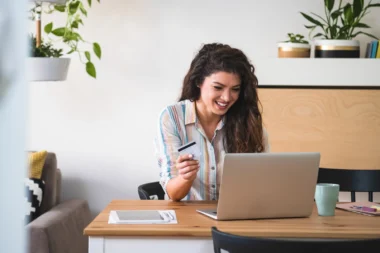Junge Frau, die mit Kreditkarte am Schreibtisch sitzt und Geld beim Online-Shopping ausgibt