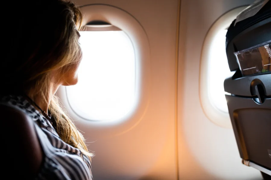 junge Frau genießt den Blick aus dem Fenster an Bord eines Flugzeugs und das Sammeln von Flugmeilen