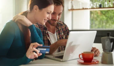 junges Paar im Wohnzimmer am Laptop beim Online-Shopping mit ihrer Kreditkarte