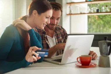 junges Paar im Wohnzimmer am Laptop beim Online-Shopping mit ihrer Kreditkarte