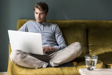 Mann sitzt querbeinig, während er Laptop benutzt