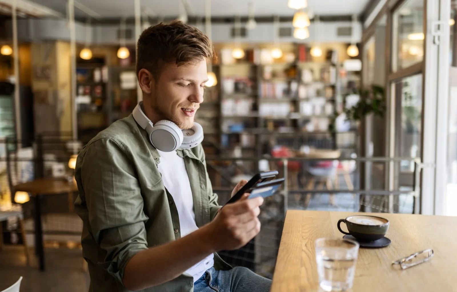 Mann sitzt in einem Cafe mit Smartphone und Kreditkarte