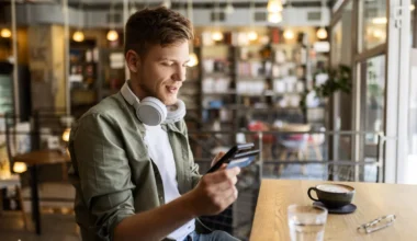 Mann sitzt in einem Cafe mit Smartphone und Kreditkarte