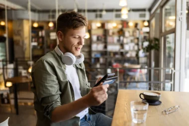 Mann sitzt in einem Cafe mit Smartphone und Kreditkarte