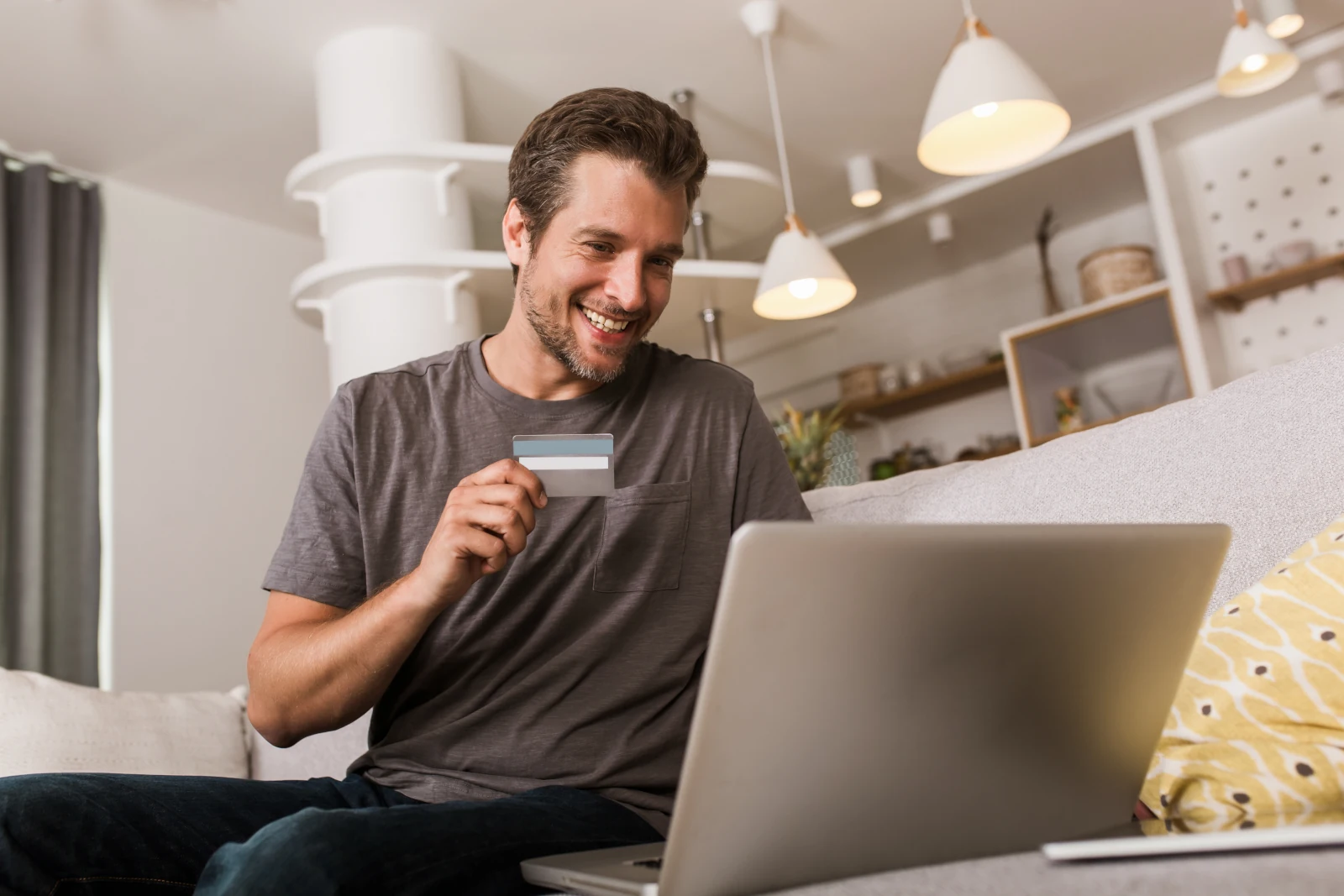 junger Mann freut sich über Online-Shopping am Laptop mit Kreditkarte