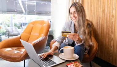 Lächelnde junge Frau, die mit Business Kreditkarte in einem Café mit Kreditkarte eine Reise bucht