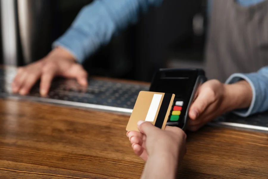 junge Frau nutzt Kreditkarte zum Bezahlen, Barkeeper hält Terminal über den Tresen