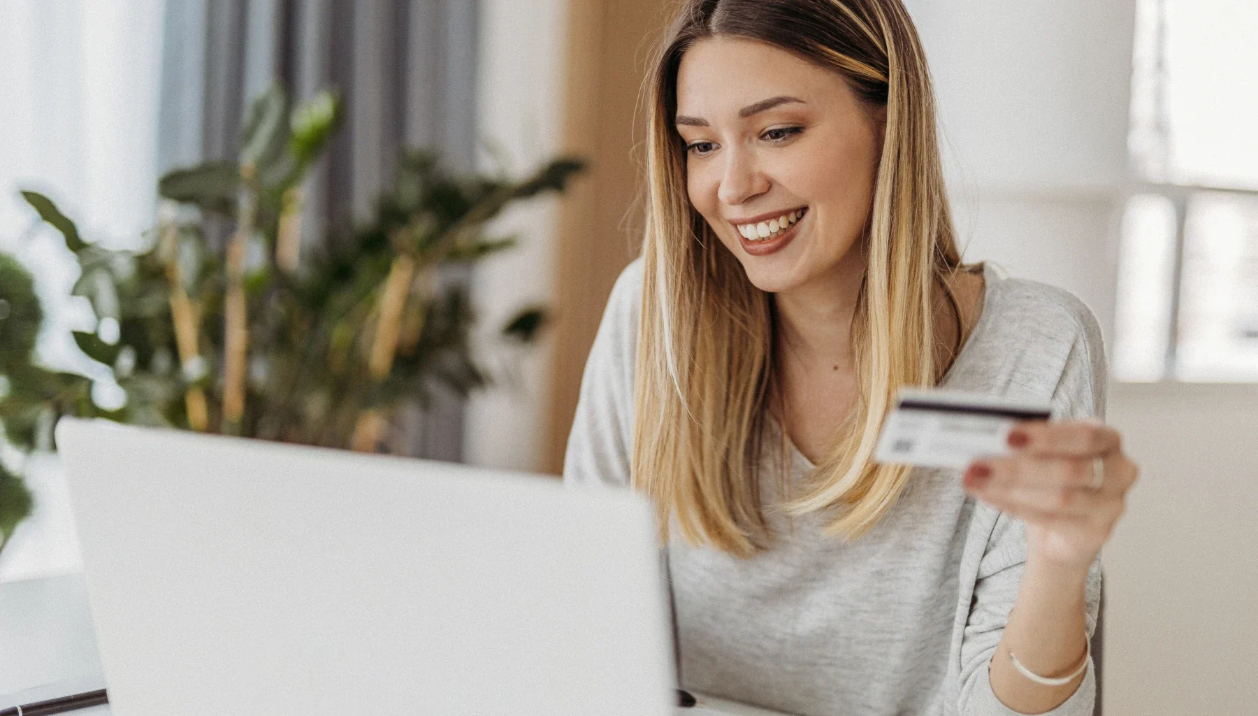 junge Frau am Laptop mit Kreditkarte freut sich über das Erreichen des Mindestumsatz und Willkommensbonus
