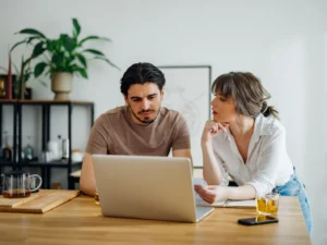 Paar erledigt gemeinsam Haushaltsfinanzen online auf einem Laptop in der Küche.