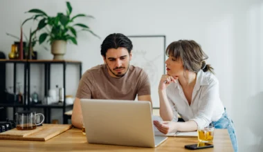 Paar erledigt gemeinsam Haushaltsfinanzen online auf einem Laptop in der Küche.
