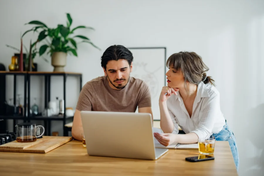 Paar erledigt gemeinsam Haushaltsfinanzen online auf einem Laptop in der Küche.